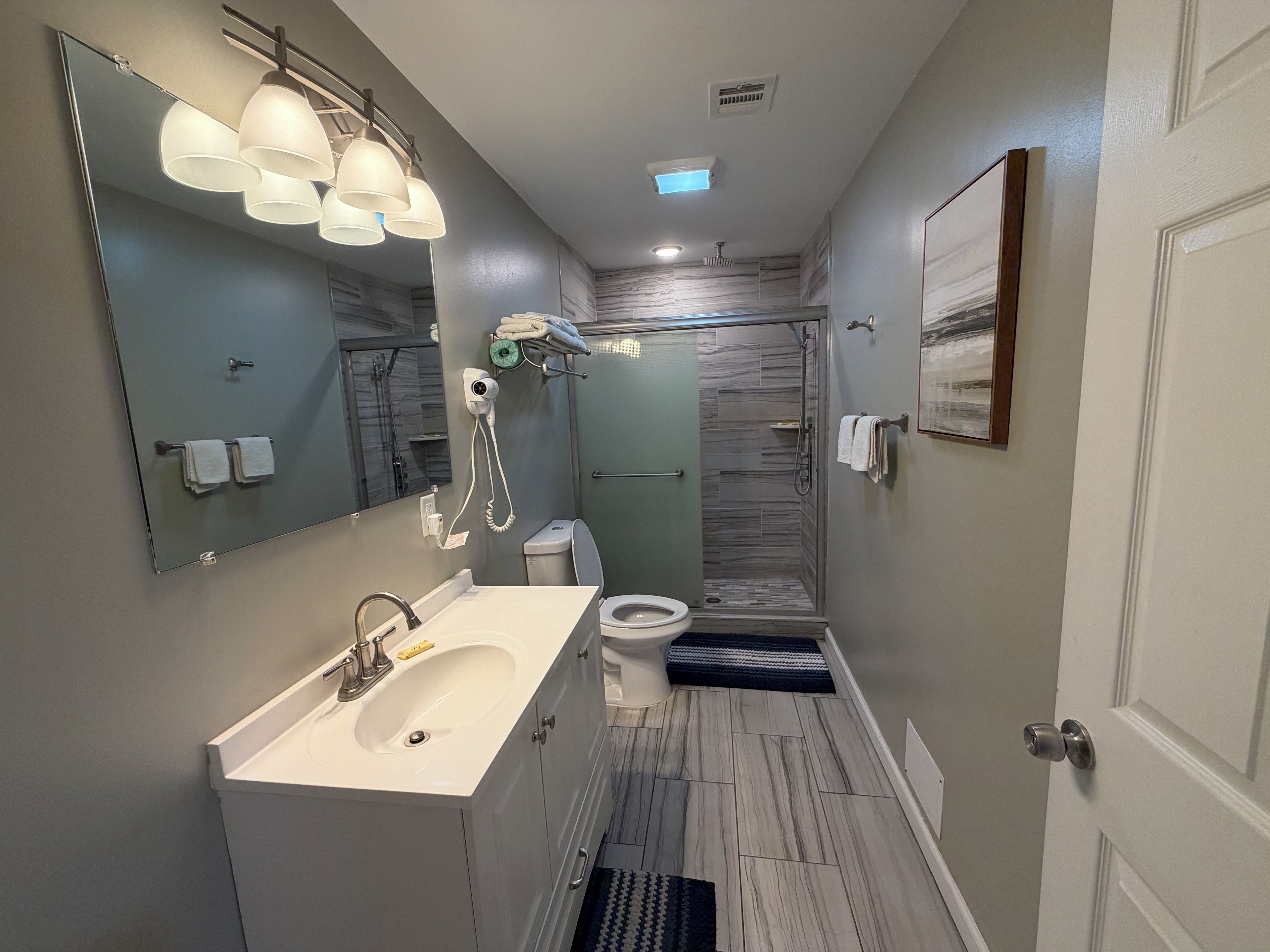 A modern bathroom with a large mirror, a sink, a toilet, and a shower area.