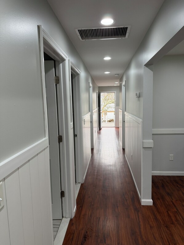 A hallway with wooden flooring, white walls, and a door leading to another room. - JD Apartments (Seaside Heights)