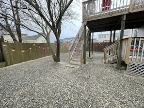 outdoor space with a deck, staircase, and gravel ground, surrounded by a wooden fence.