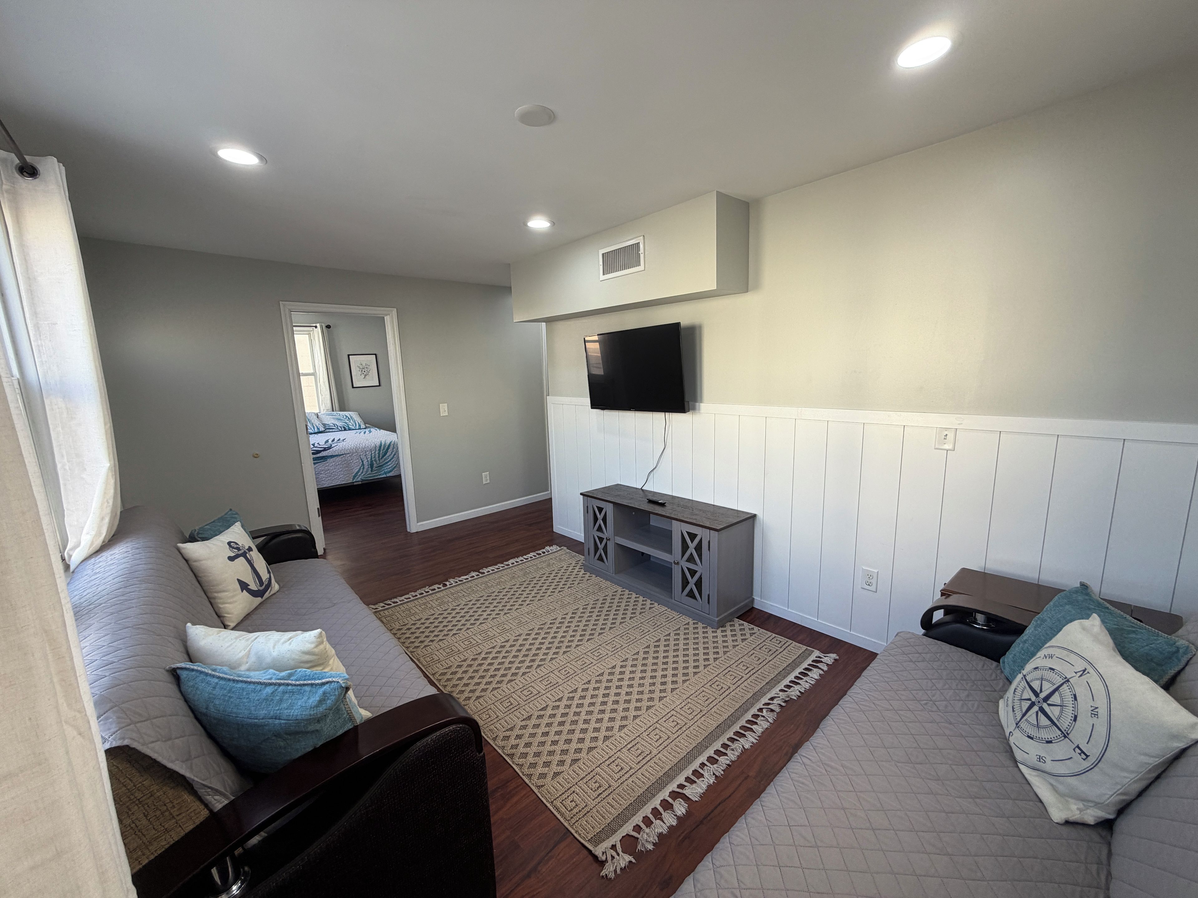 A modern living room with a sofa, a coffee table, a TV mounted on the wall, and a patterned rug.