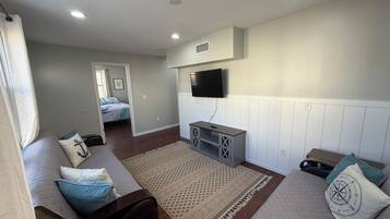 A modern living room with a sofa, a coffee table, a TV mounted on the wall, and a patterned rug.