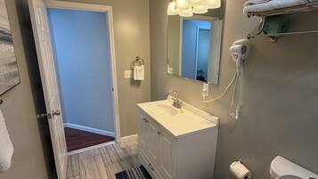 Un baño con lavamanos blanco, espejo, toallero, secador de pelo y retrete.