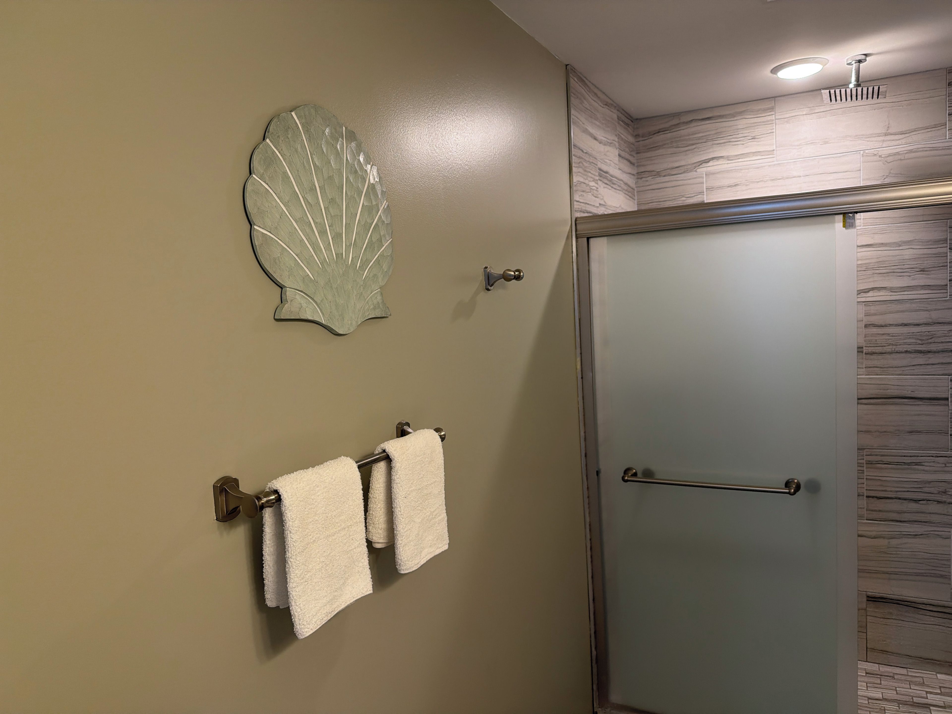Ein Badezimmer mit einer Duschkabinentür aus Glas, einem Handtuchhalter mit zwei weißen Handtüchern und einem dekorativen Wandbild mit Muscheln.