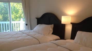 Een hotelkamer met twee bedden, een balkon en een nachtkastje met een lamp.
