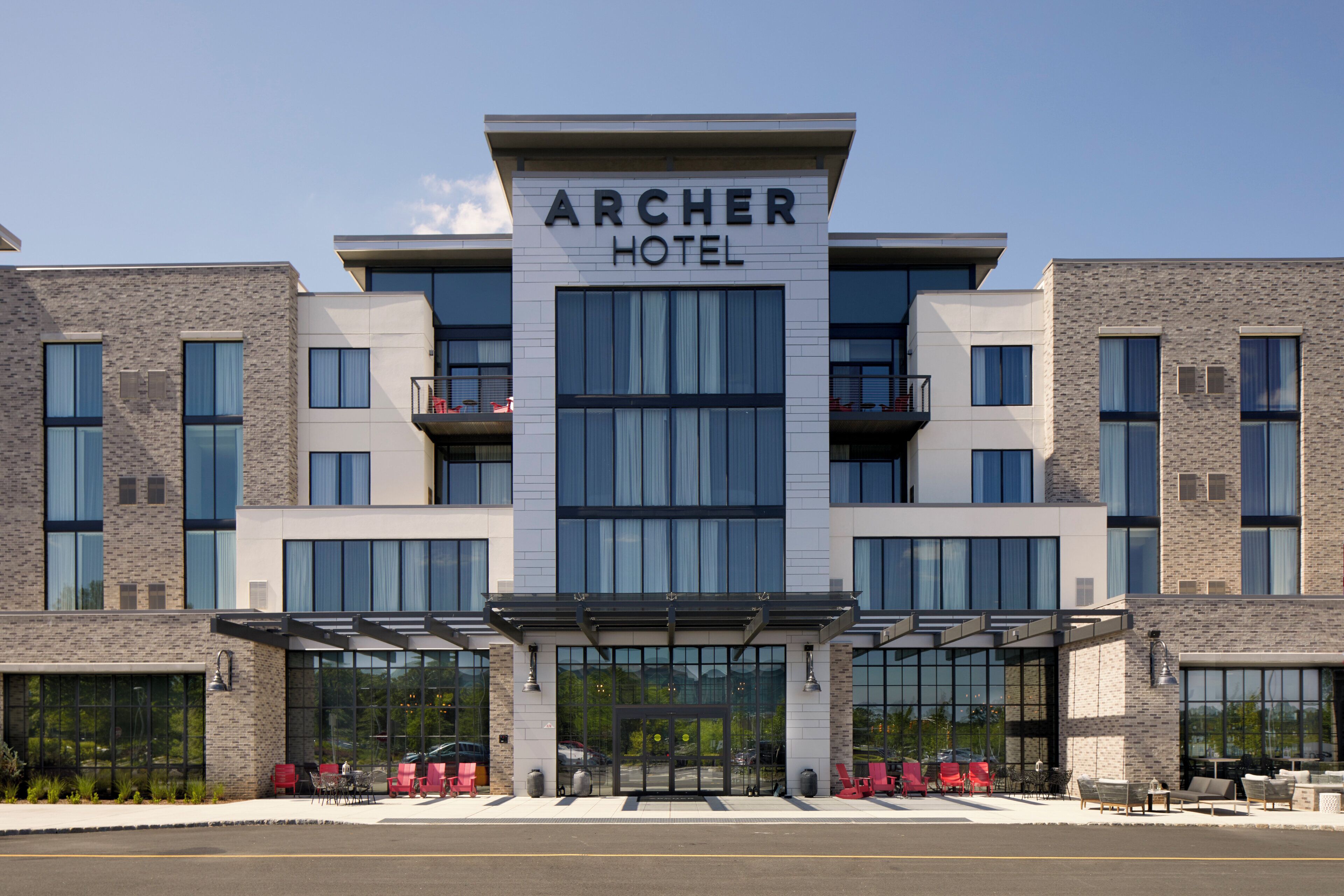 A modern hotel with a prominent sign reading "ARCHER HOTEL". It features a symmetrical facade with large windows and balconies.