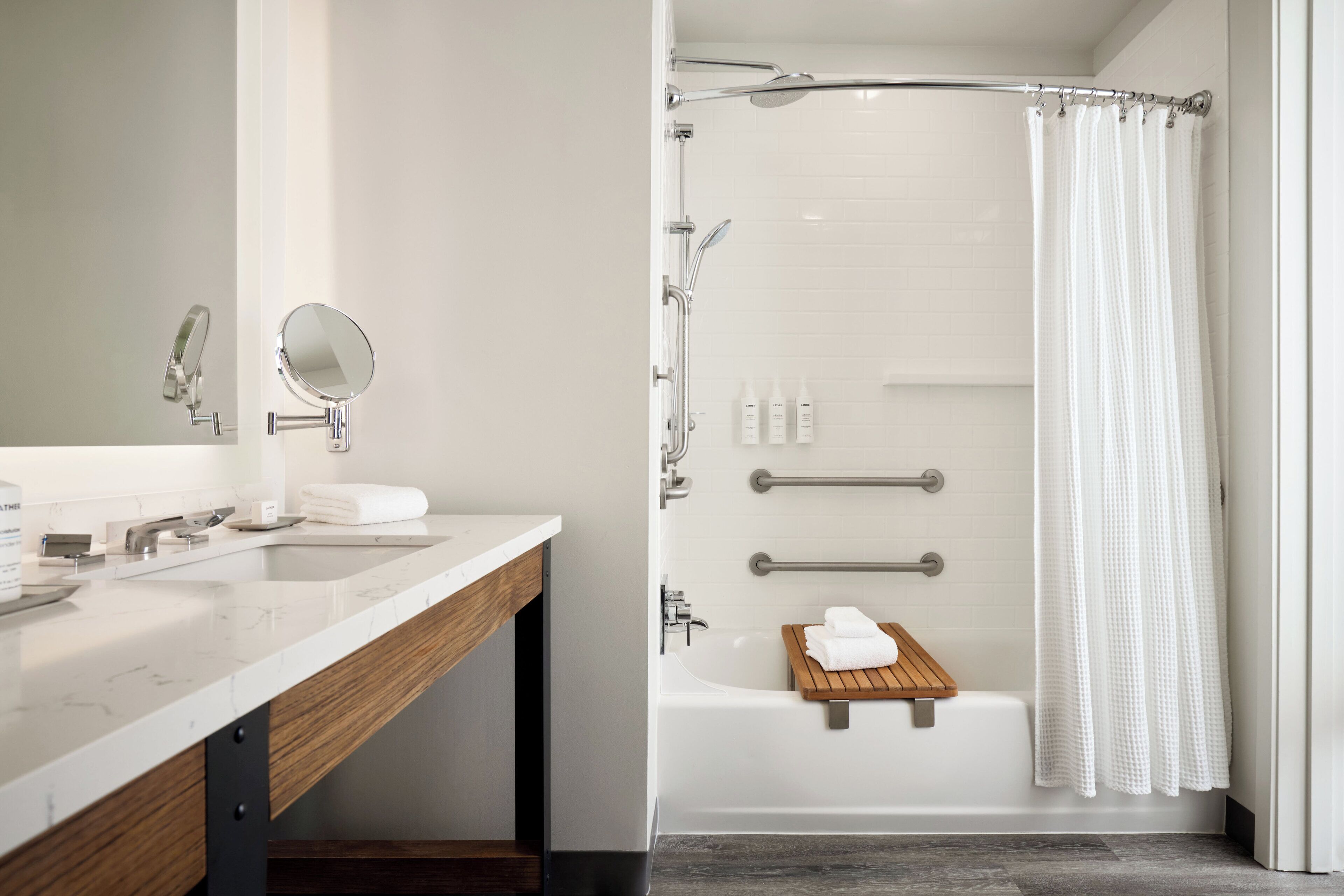 A modern bathroom with a marble vanity, a shower with a glass door, and a wooden bath tray.