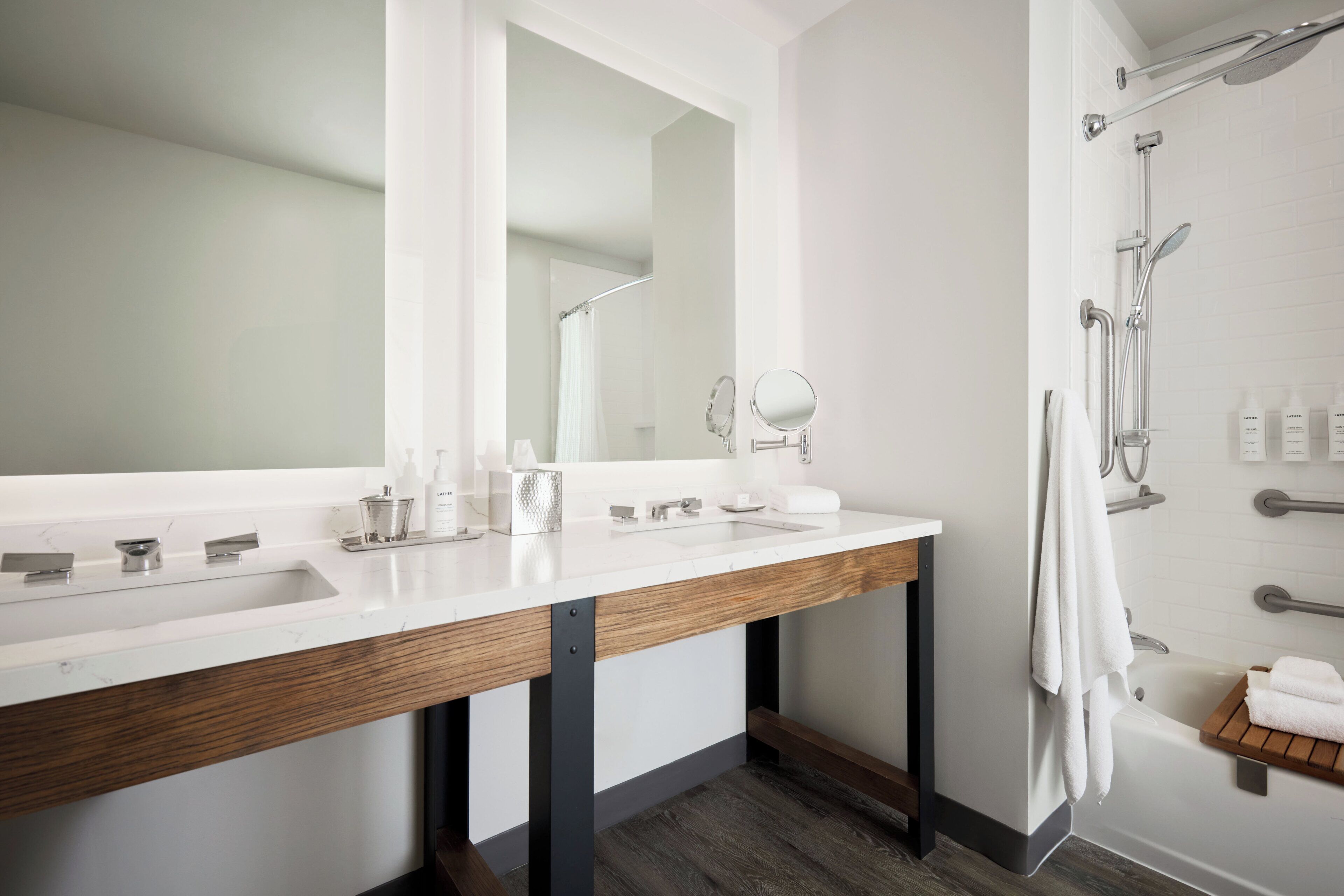 Un baño moderno con lavamanos doble, un espejo grande, una ducha con puerta de cristal y un estante de madera con toallas.