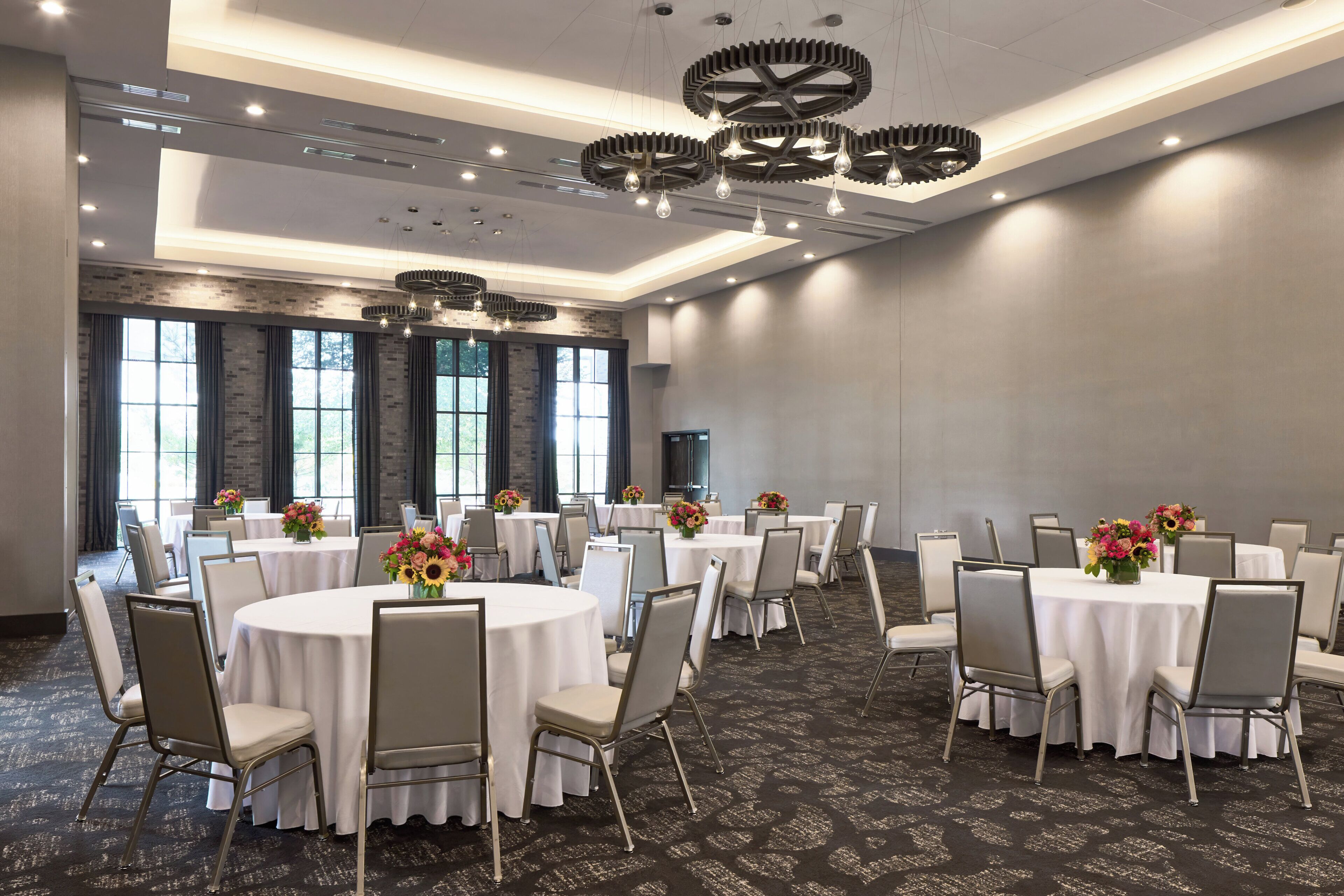 Un salón de conferencias con mesas redondas, sillas y centros de mesa con flores.