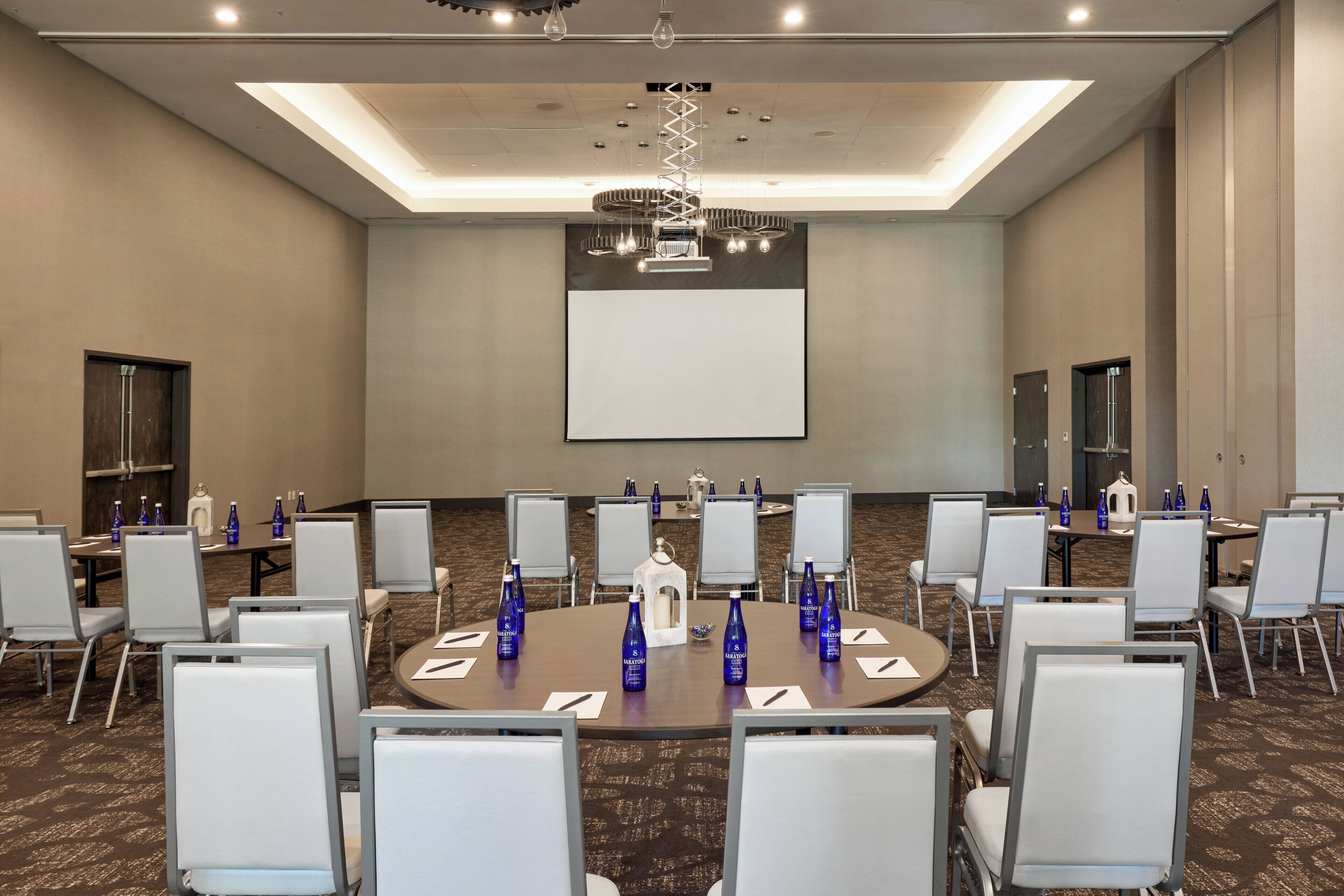 A conference room with round tables, white chairs, and blue water bottles.