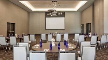 A conference room with round tables, white chairs, and blue water bottles.