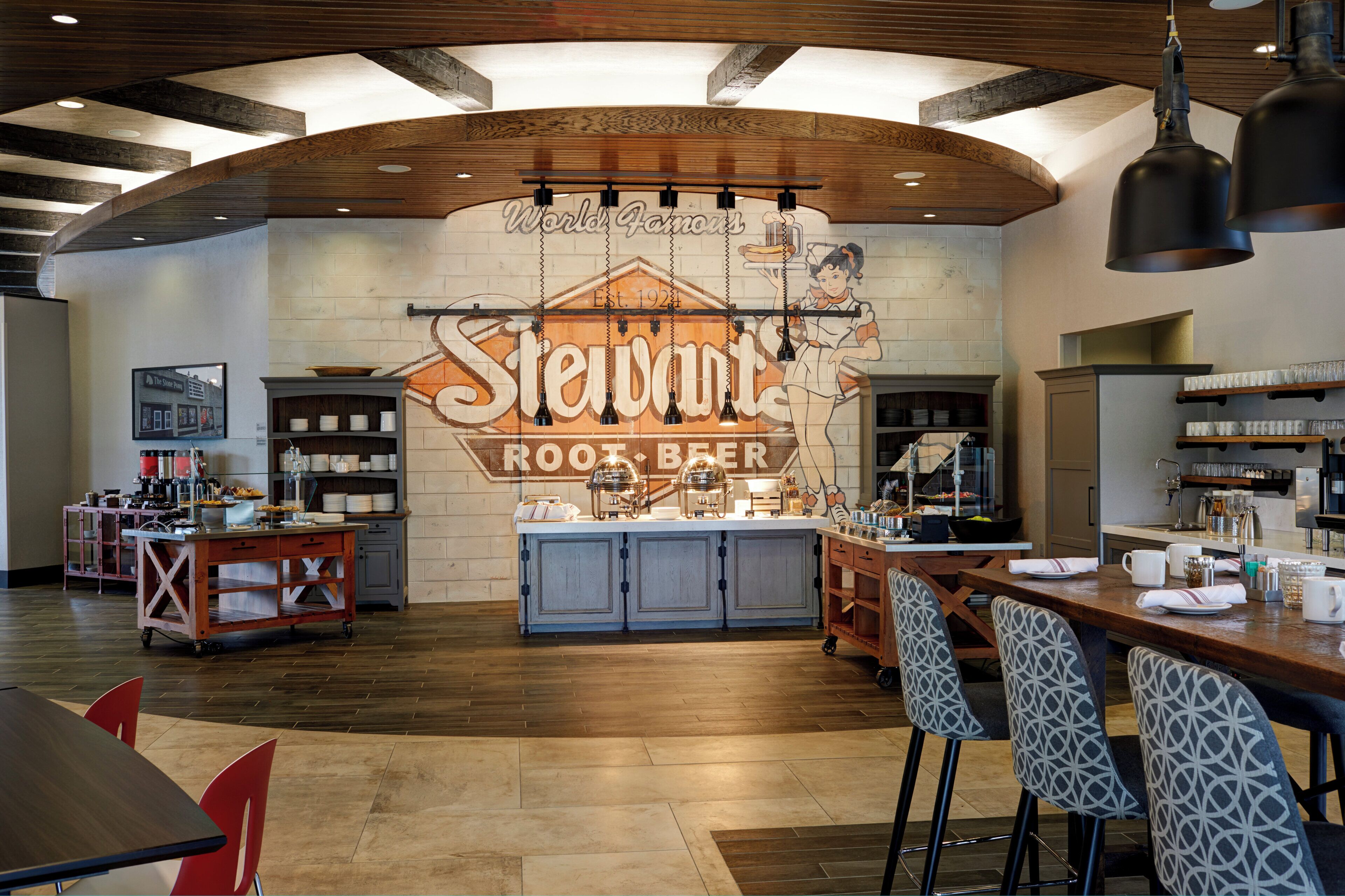 Un restaurante con un letrero grande que dice 'Stewart's Root Beer' y una zona de bar con taburetes.