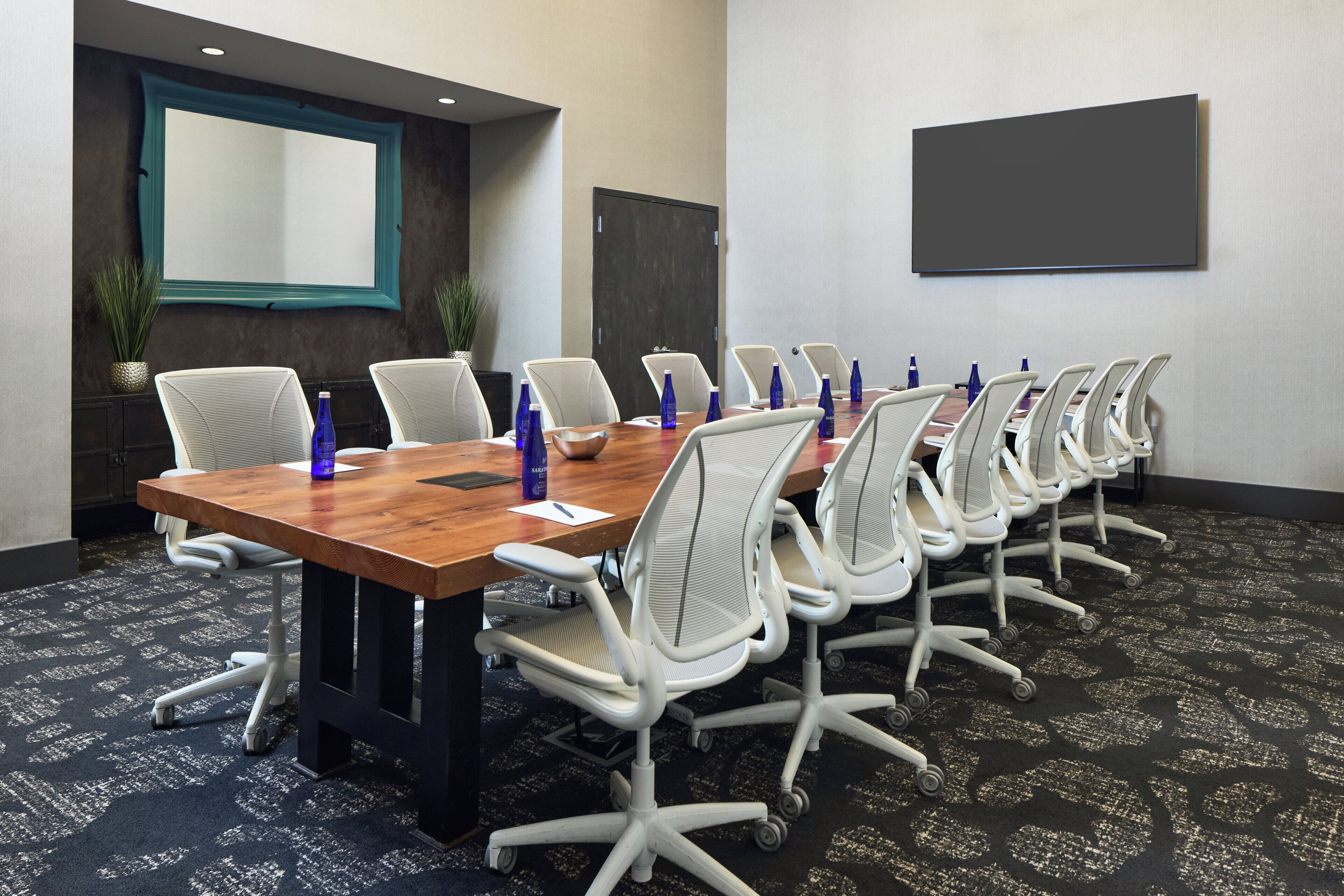 A conference room with a long table, white chairs, and a large screen.