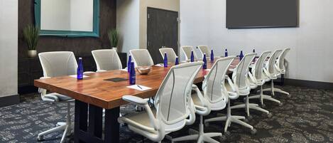 A conference room with a long table, white chairs, and a large screen.