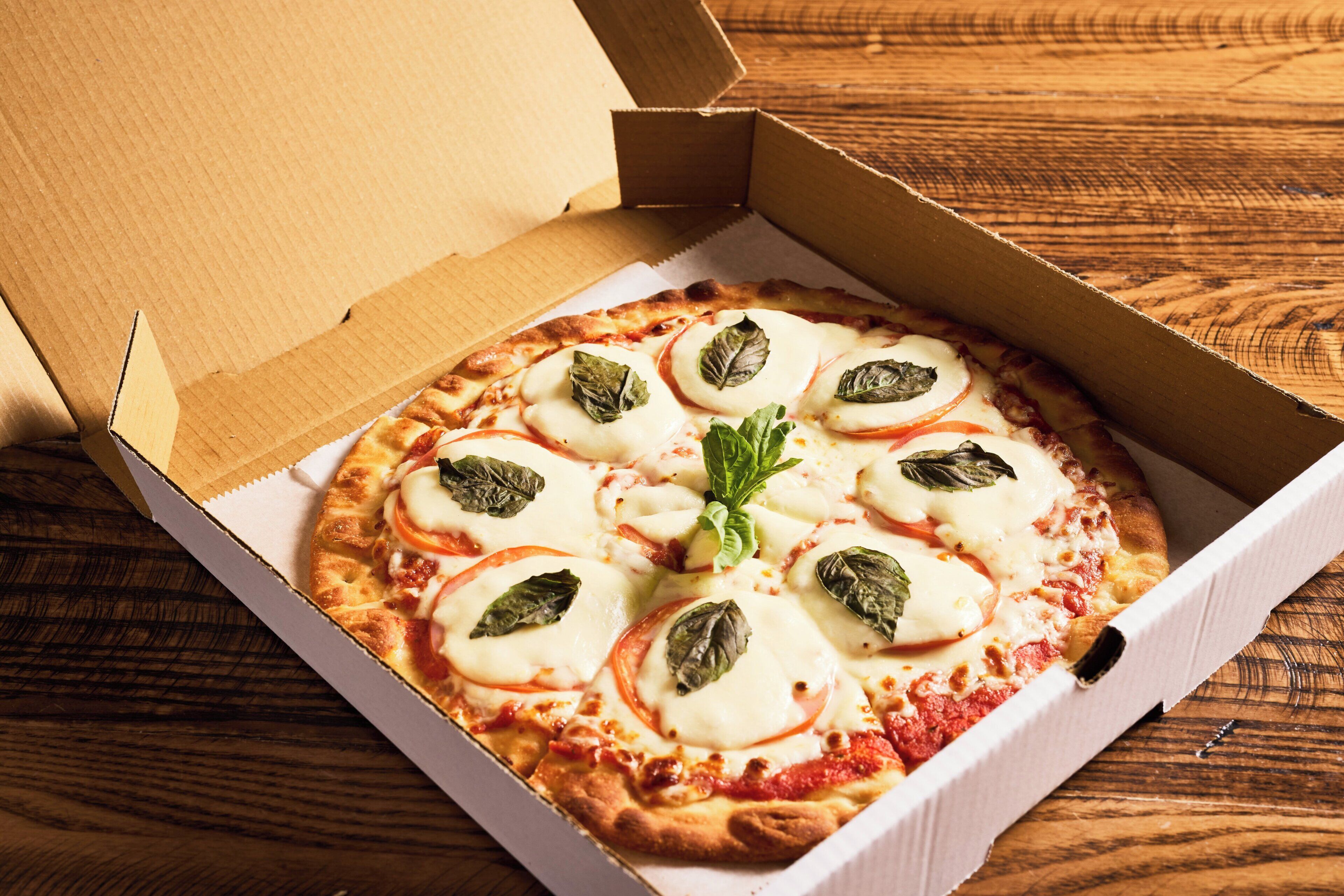 A pizza in a cardboard box on a wooden surface.