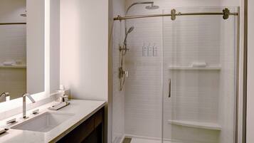 A modern bathroom with a glass-enclosed shower, a large mirror, and a white sink.