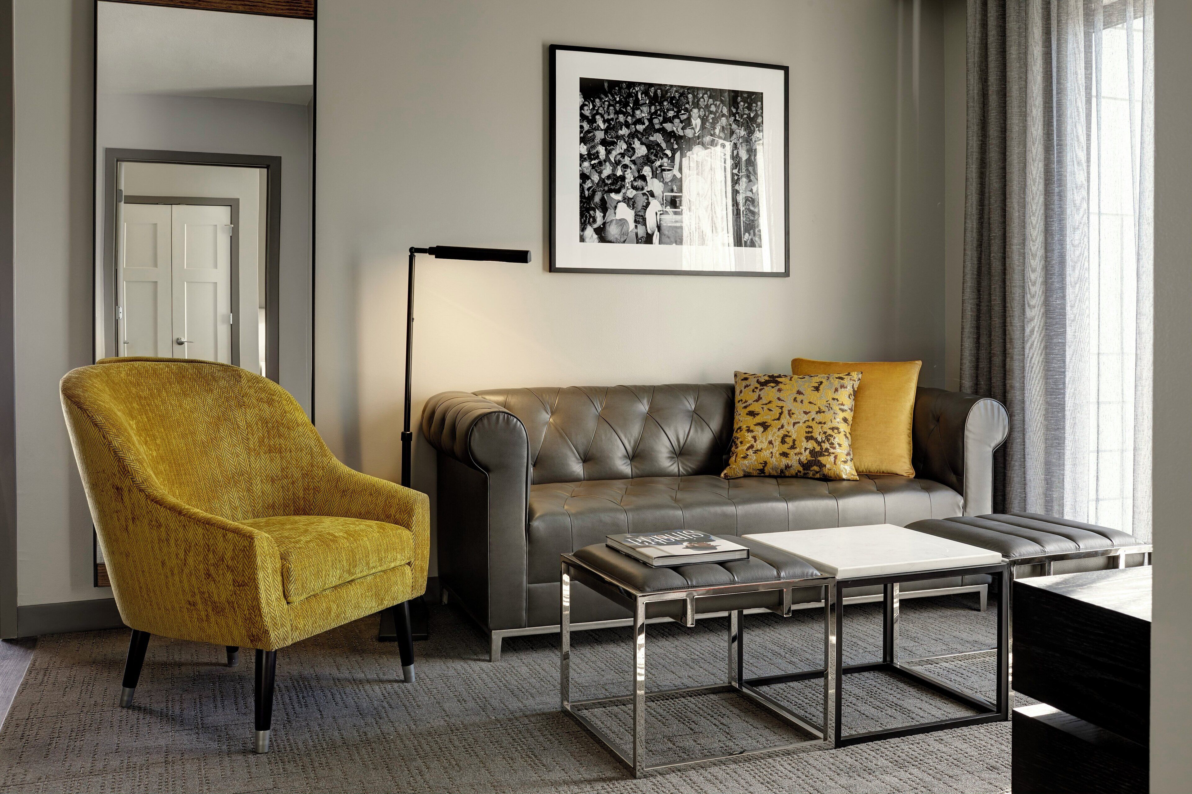 Een moderne woonkamer met een gele fauteuil, een grijze bank met gekleurde kussens en een salontafel.