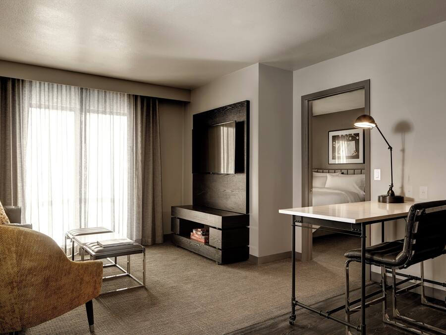 A hotel room with a sofa, a desk with a chair, a TV, a bedside table, and a mirror.