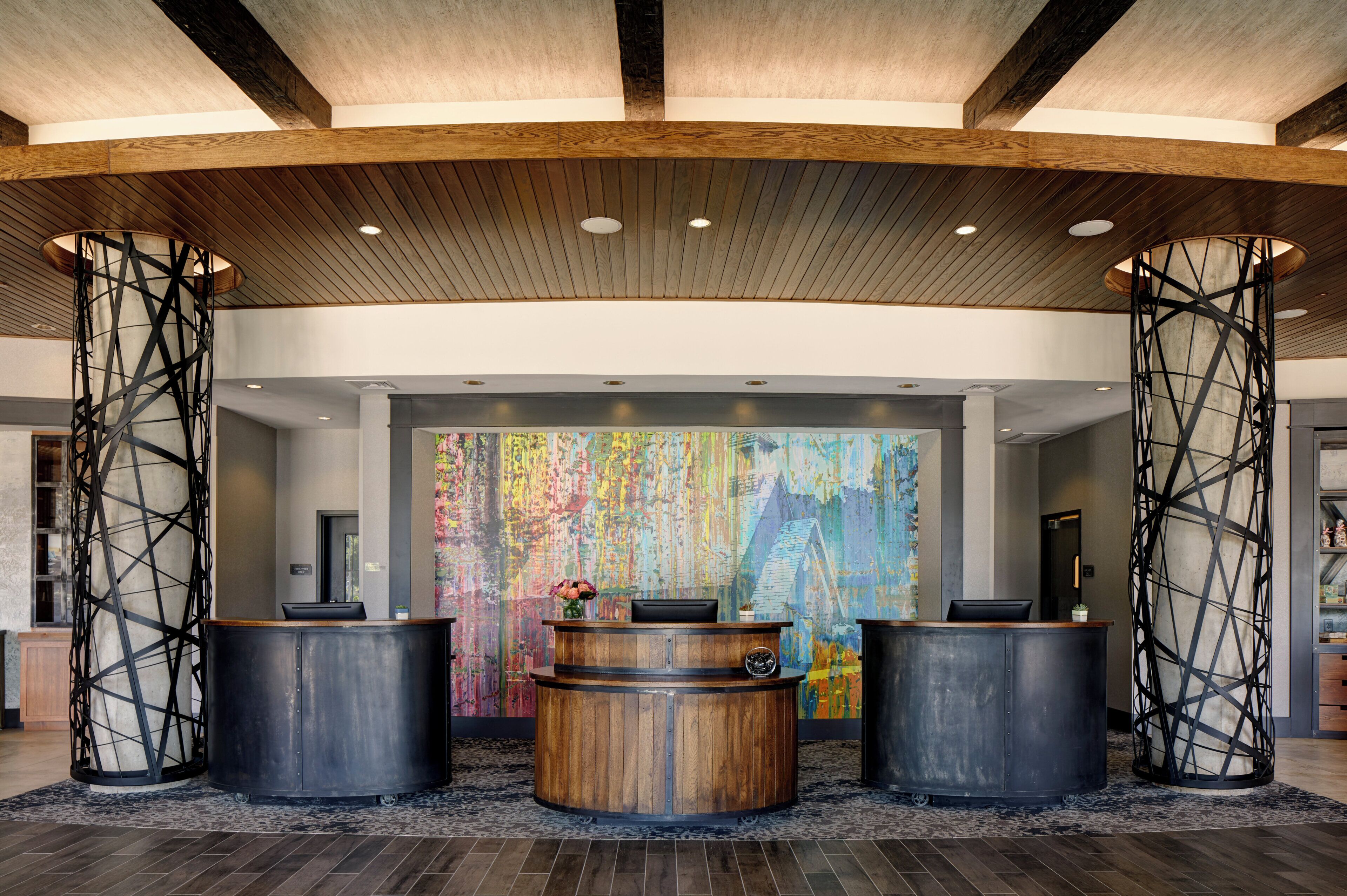 A reception area with a wooden reception desk, two tall black columns, and a colorful abstract mural on the wall.