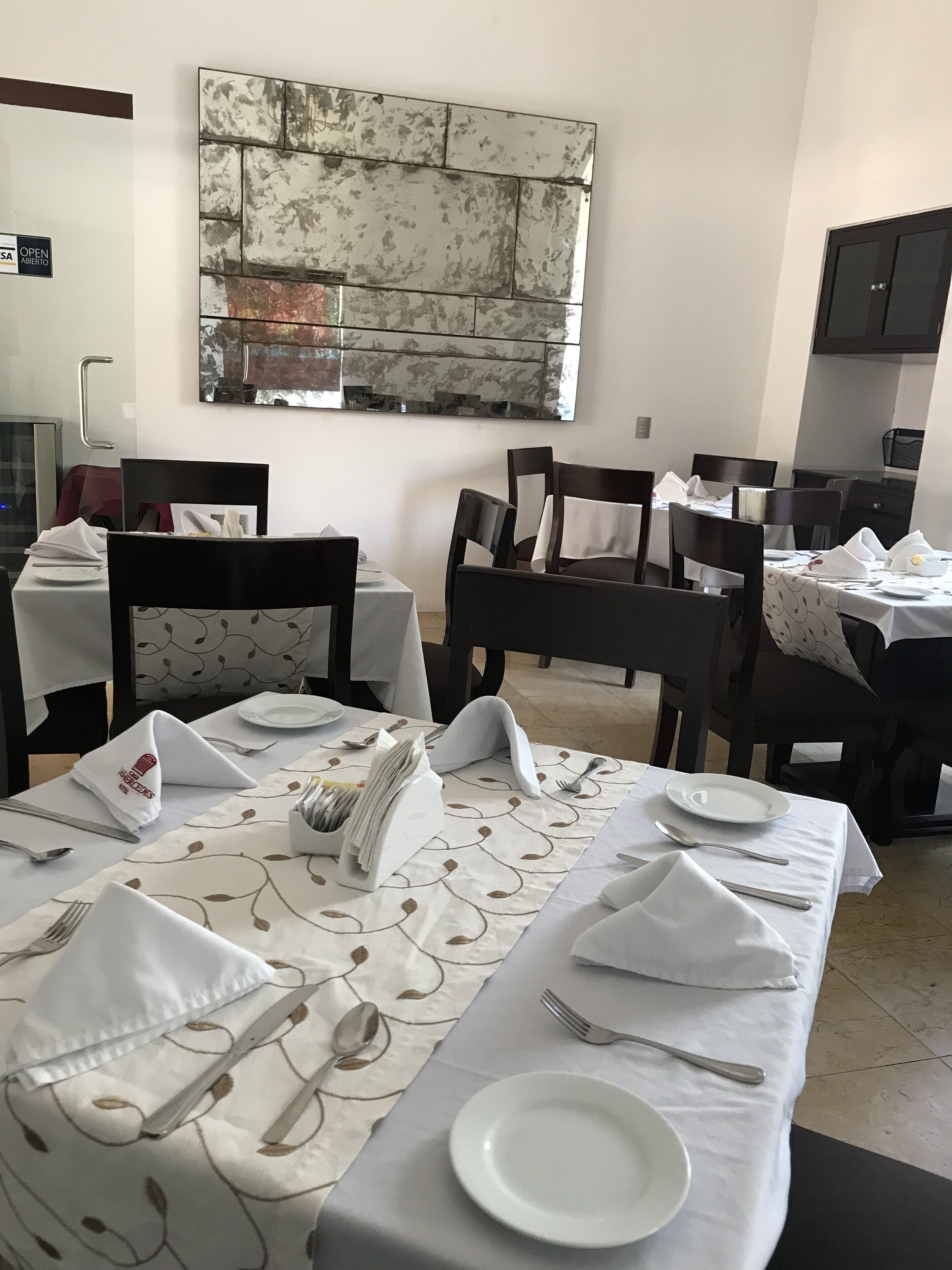 Comedor con mesas dispuestas para cuatro comensales, cada una con mantel blanco y cubiertos ordenados.