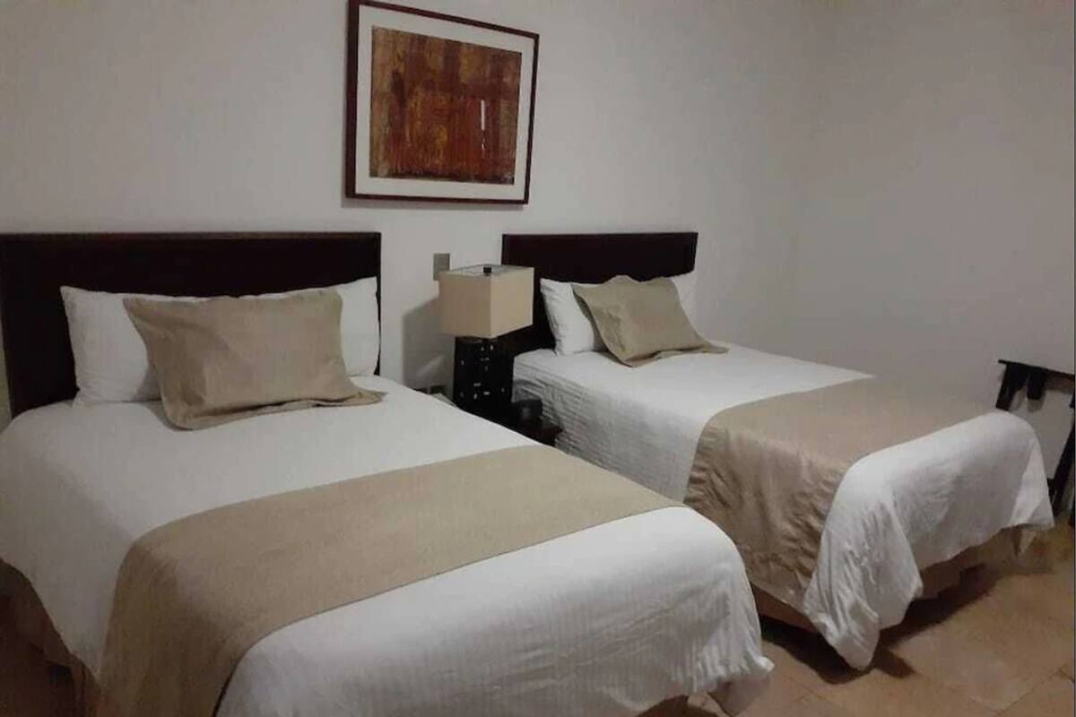 Deux lits simples avec des têtes de lit, une table de chevet avec une lampe et un tableau encadré au mur.
