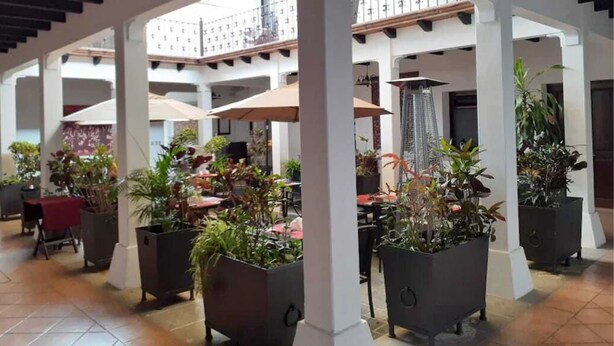 A covered outdoor area with multiple seating areas, potted plants, and umbrellas. - Hotel Casa las Mercedes (Oaxaca)