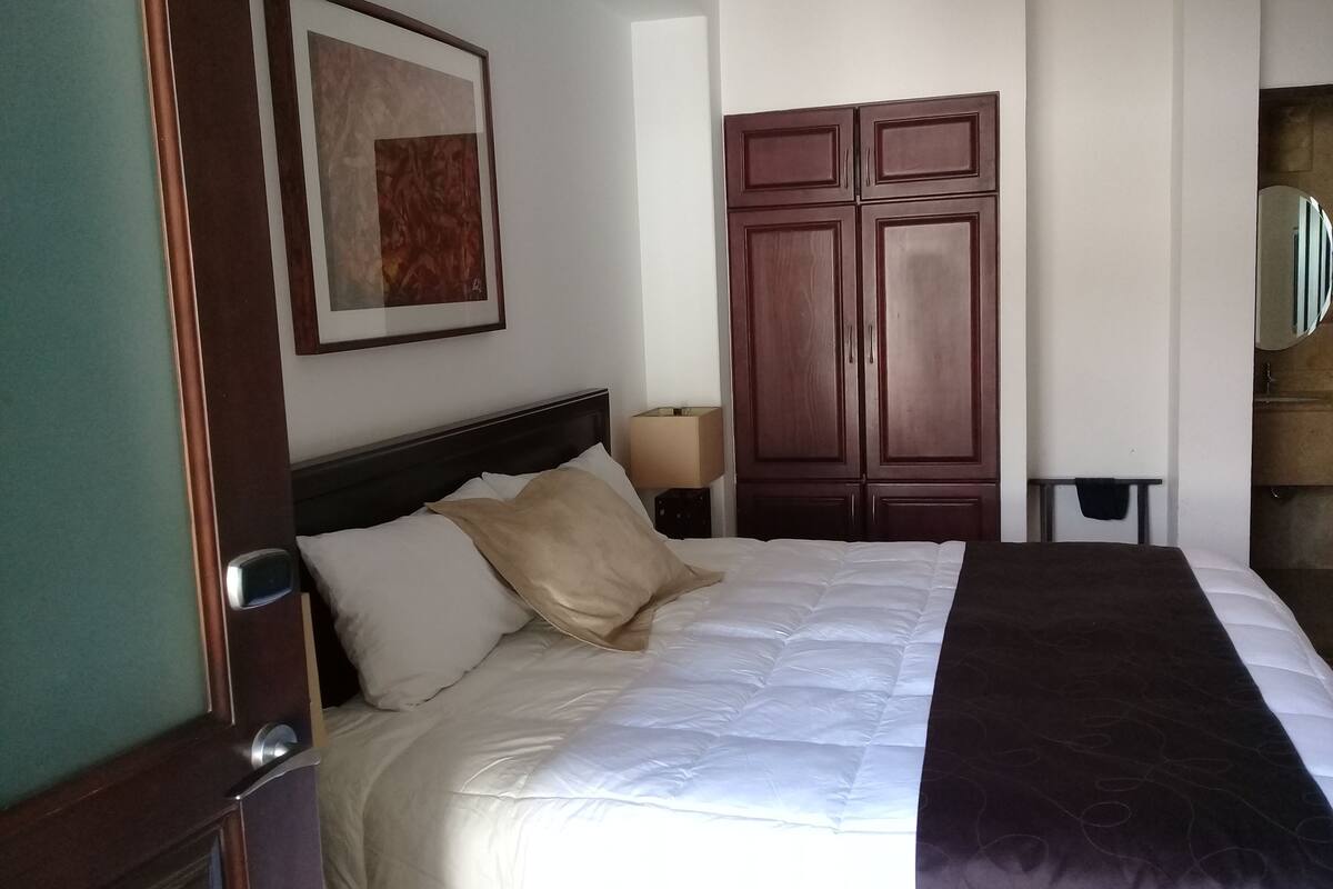 Une chambre d’hôtel avec un lit, une armoire, un tableau encadré au mur et une table de chevet avec une lampe.
