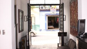 An interior space with a doorway leading to a street, a chair, a television, and a door with a sign. - Hotel Casa las Mercedes (Oaxaca)