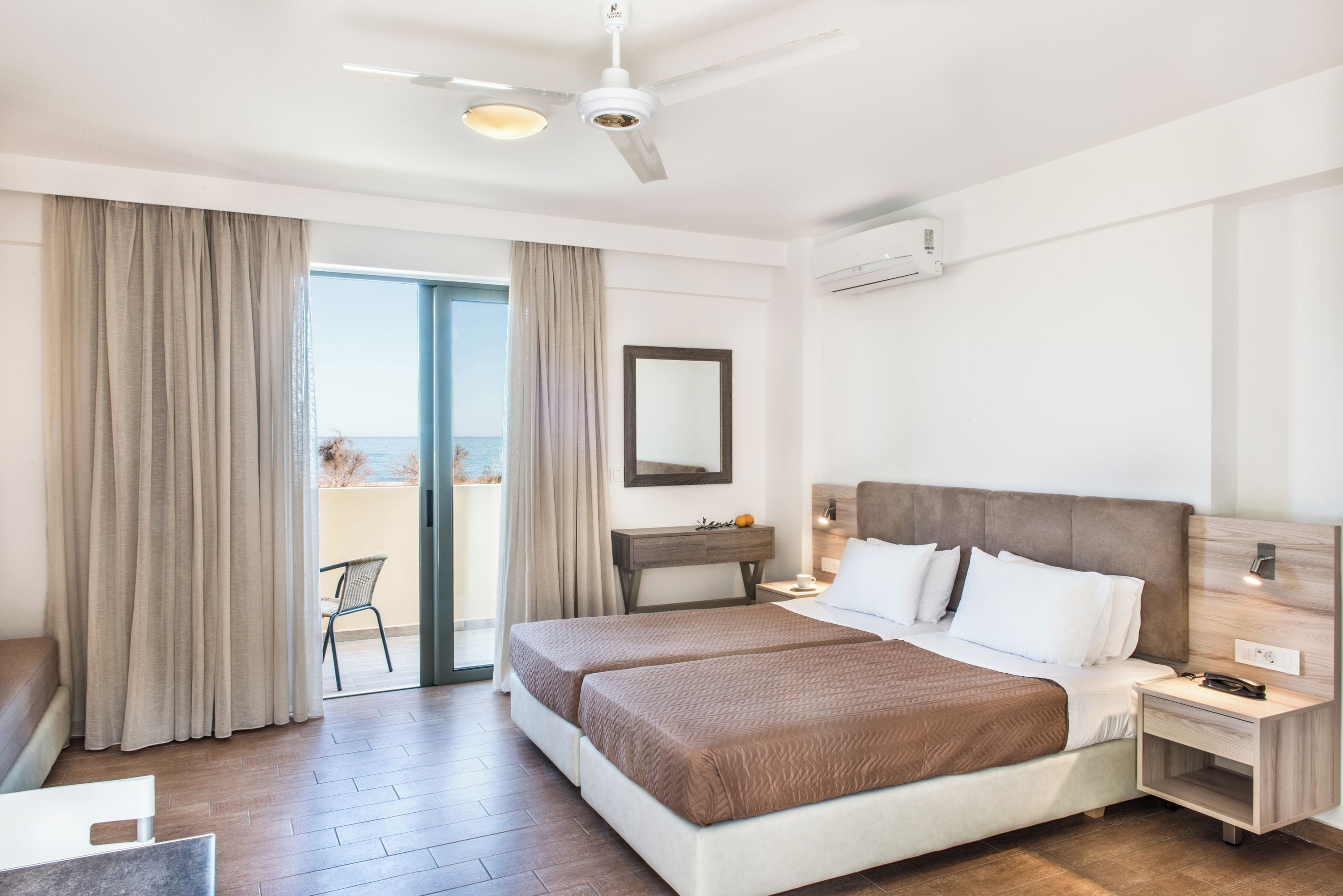 A hotel room with a bed, a desk, a chair, and a view of the sea.