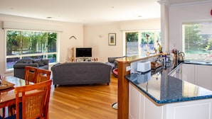 A spacious living area with a sofa, dining table, and chairs, a kitchen with a countertop, and large windows offering views of the outdoors. - Lochnagar Barossa - Adults Only (Tanunda)