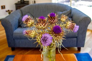 Un jarrón con flores moradas sobre una mesa de madera en una habitación con un sofá azul y suelo de madera.