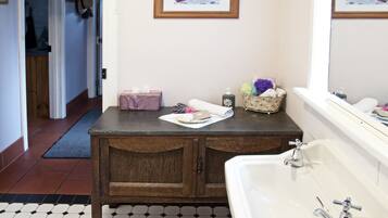 A bathroom with a white sink, wooden vanity, and a tiled floor. There is a framed picture on the wall and a mirror above the sink.