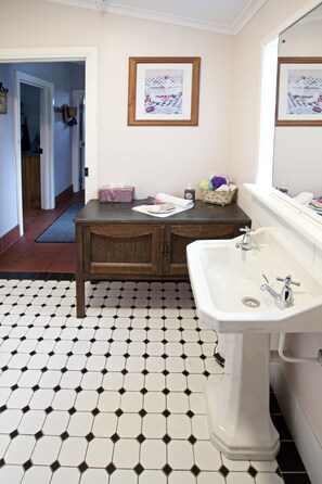 A bathroom with a white sink, wooden vanity, and a tiled floor. There is a framed picture on the wall and a mirror above the sink.