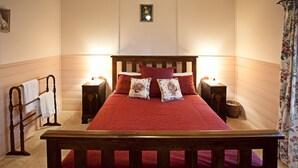 Una cama con estructura de madera, ropa de cama roja y dos mesitas de noche con lámparas.