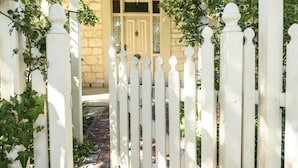 Une clôture blanche faite de piquets de bois mène à un bâtiment doté d’une porte et de fenêtres.