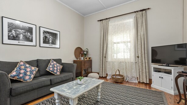A living room with a sofa, a coffee table, a television, and framed pictures on the wall. - Miriams Cottage (Tanunda)