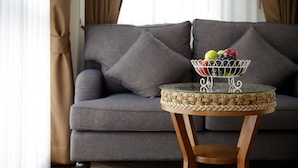 A round glass table with a woven edge, placed on a wooden base, in front of a grey sofa with two cushions. - 9 Suite Luxury Boutique Hotel (Chiang Mai)