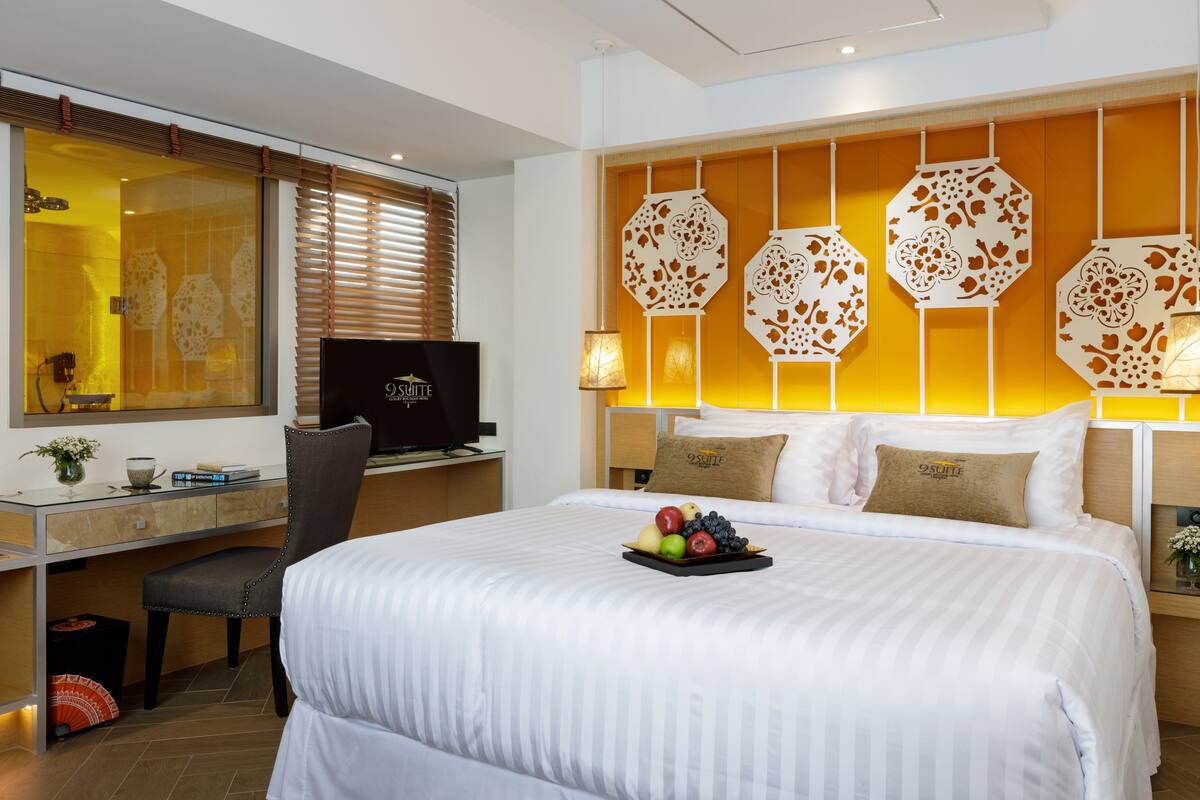 A hotel room with a large bed, a desk with a computer, and decorative wall panels.