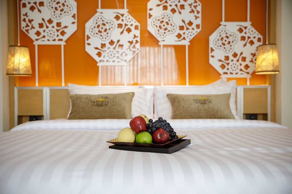 Ein Hotelzimmer mit Bett, Kissen, Obstkorb und dekorativen Wandpaneelen.