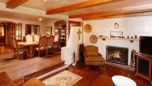 A spacious living room with a fireplace, wooden beams, a dining area with chairs, and a television.