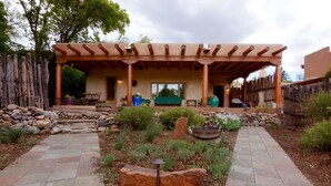 A covered patio area with a rustic wooden pergola, stone pathway, and outdoor seating.