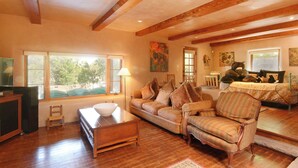 A spacious living room with wooden beams, a sofa, a chair, and a television.