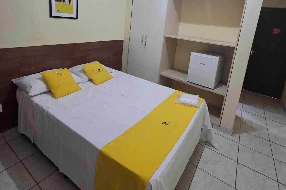 A hotel room with a bed, a wardrobe, a desk, and a painting on the wall.