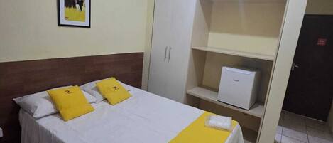Una habitación de hotel con cama, armario, escritorio y un cuadro en la pared.
