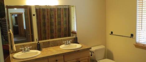 A bathroom with two sinks, a toilet, a mirror, and a window with blinds.