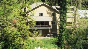 A two-story building with a balcony, surrounded by dense greenery and a body of water. - McKenzie Riverfront-w Hottub woodstove+wood (Vida)