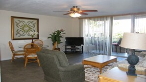 Un salon avec un ventilateur de plafond, un téléviseur, une table à manger avec des chaises, un canapé et une plante en pot.