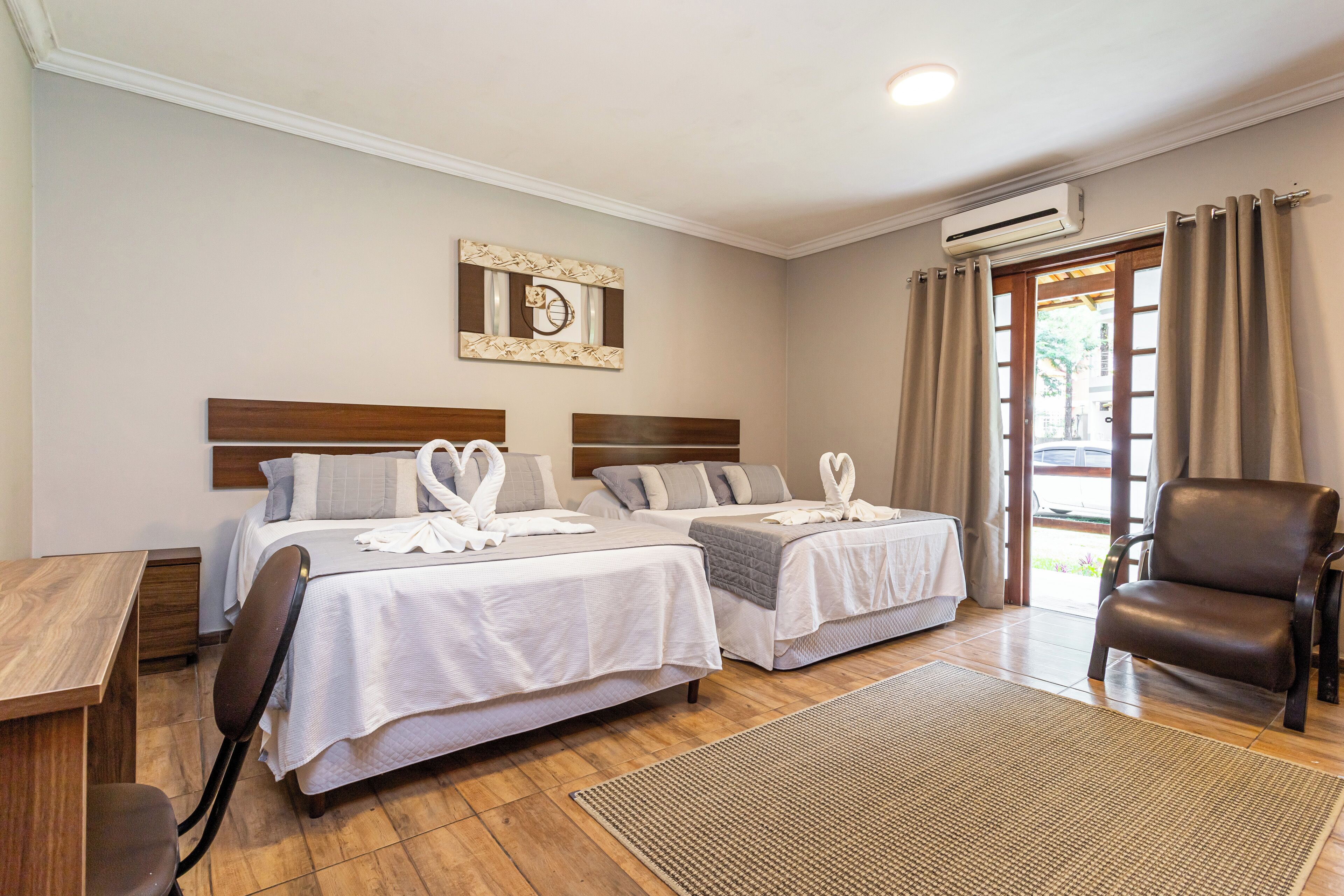 Habitación de hotel con dos camas, un escritorio de madera, una silla de cuero marrón y un ventanal con cortinas.