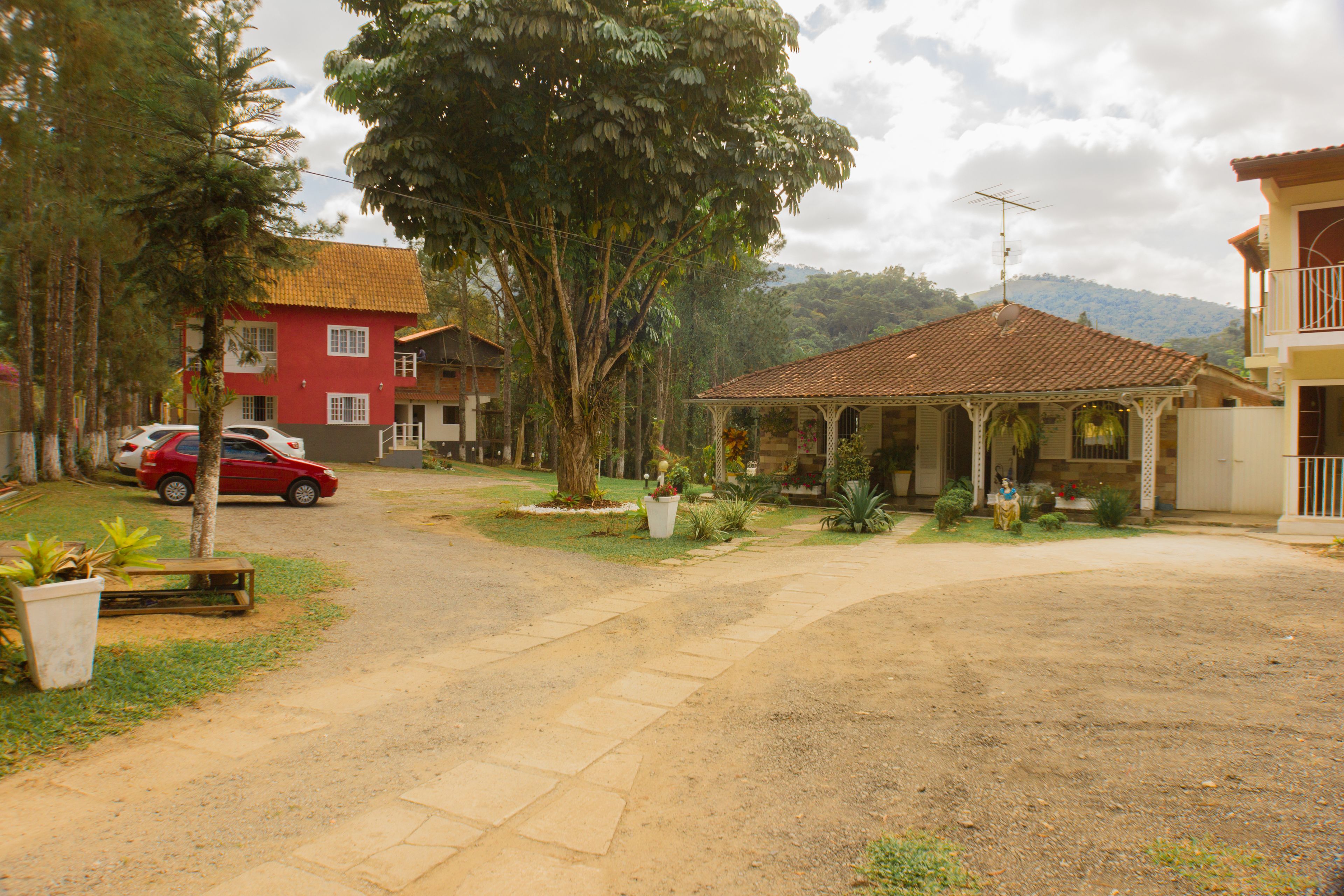 A residential area with a red car parked on the street, a gazebo, and houses with visible balconies.