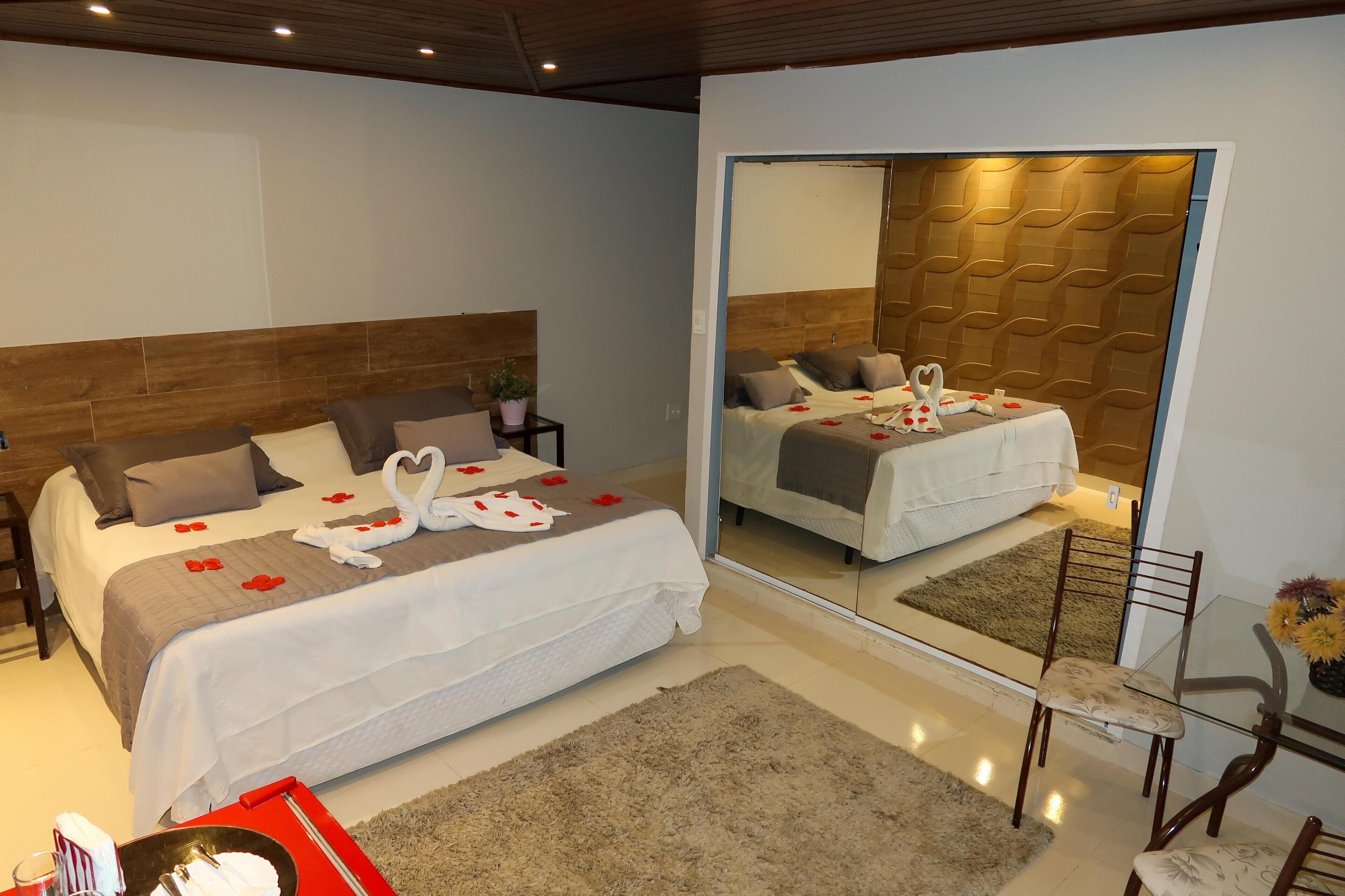 Quarto de hotel moderno com uma cama grande, um espelho, uma pequena mesa e uma cadeira.