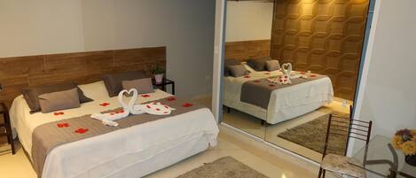 A modern hotel room with a large bed, a mirror, a small table, and a chair.